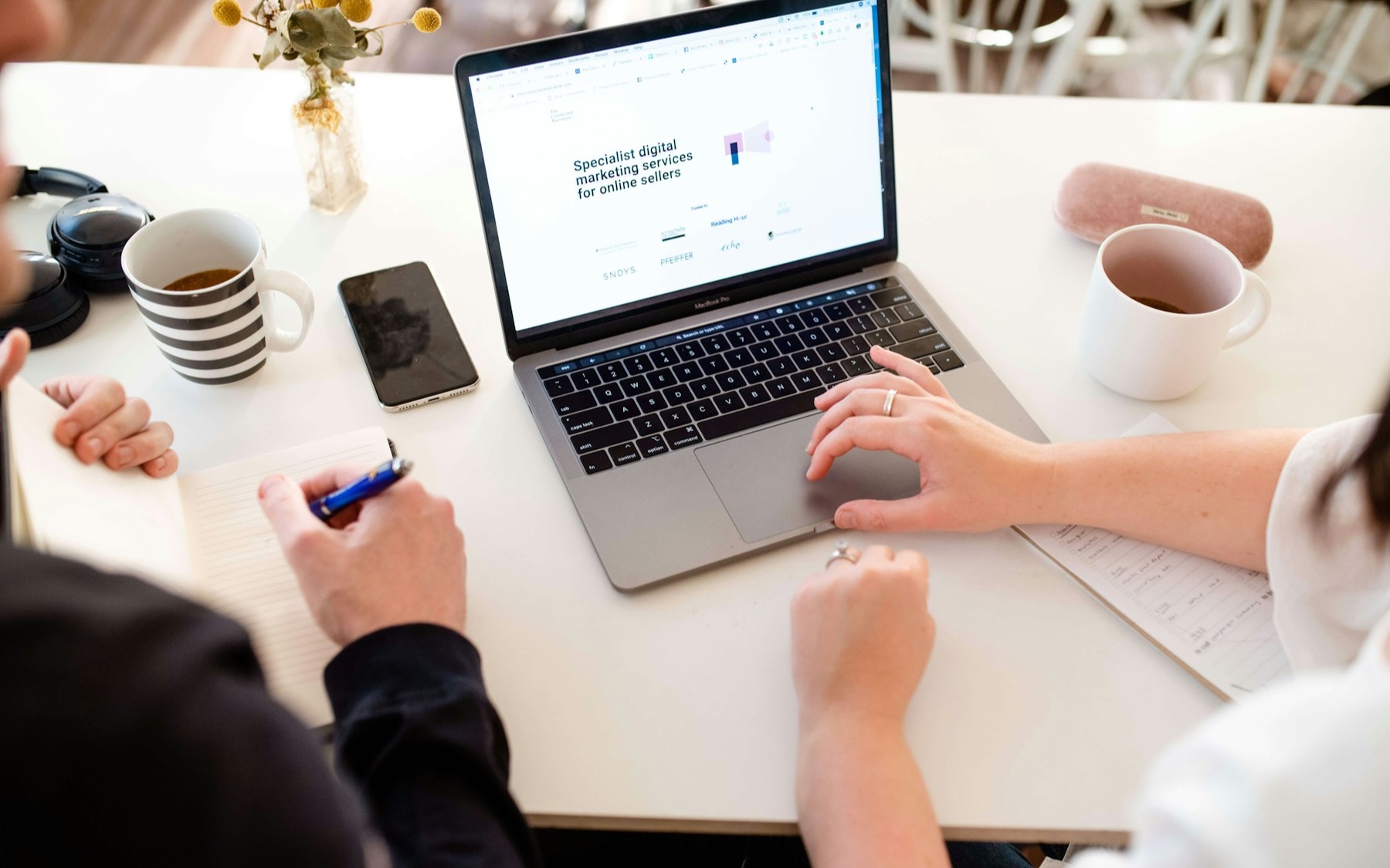 Hands working across a laptop and notebook in a founder meeting.